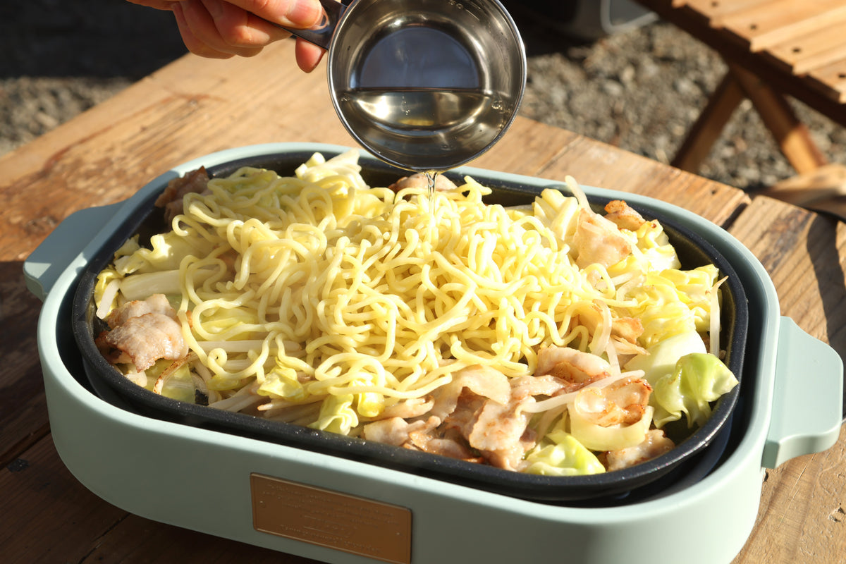 麺を加えて酒を入れ、蓋をして蒸し焼きにしている様子